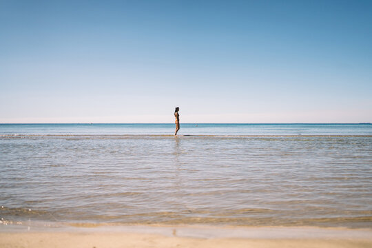 Wide minimal view of a woman standing in shallow sea water on a peaceful summer day