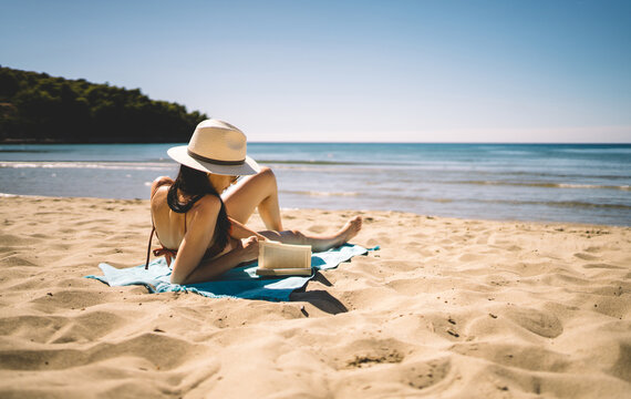 Woman reading book while relaxing on sandy beach