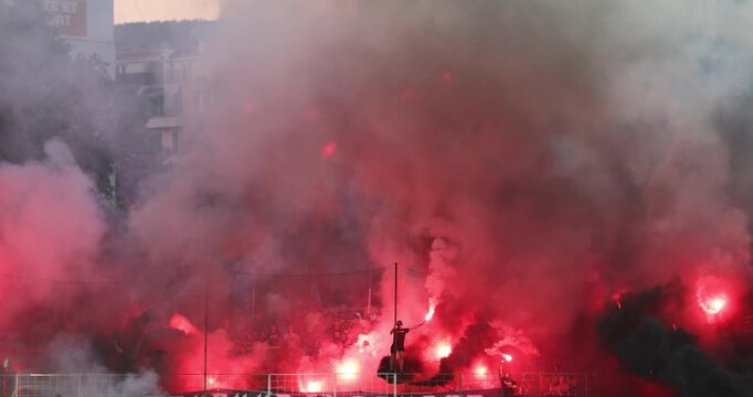 Passionate football fans with smoke bombs, fire torch and flares at a stadium. Ultras creating an intense, chaotic atmosphere with pyrotechnics during a night match or protest.