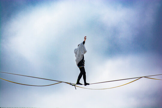 Brave tightrope walker balancing on a slackline high in the sky against cloudy background