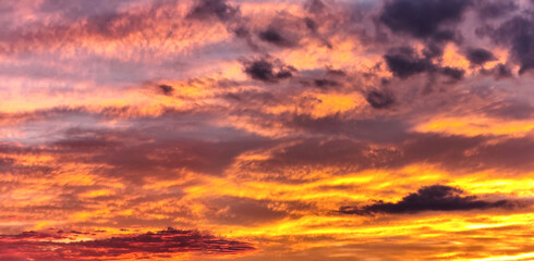 Fototapeta premium Vivid dramatic sunset sky with golden orange, pink and purple clouds, colorful evening cloudscape at dusk, beautiful natural background with warm glowing light and deep blue tones