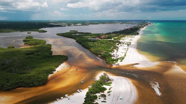 Rusty tidal channels cut across pale sandbars beside a lively resort shoreline dotted with anchored day boats and patchy sun.