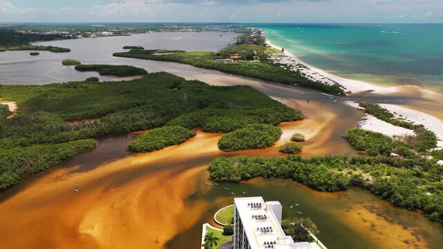 Sediment-rich channels curl past dense islands and sand flats near a waterfront high-rise on a busy summer coastline.