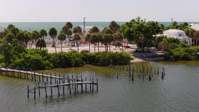 Old wooden docks jut into a calm Florida bay beside palm-lined streets and waterfront homes under clear midday light.