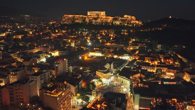 Breathtaking aerial footage of the illuminated Athens cityscape at night, featuring the majestic Acropolis and Parthenon standing prominently against the dark sky over the sprawling urban lights