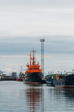 Orange industrial tugboat moored in a harbor with a tall communication tower under a cloudy sky