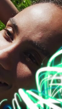 Vertical video: Woman lying on grass neon sweeping right urging eye open and hair tucking for tech