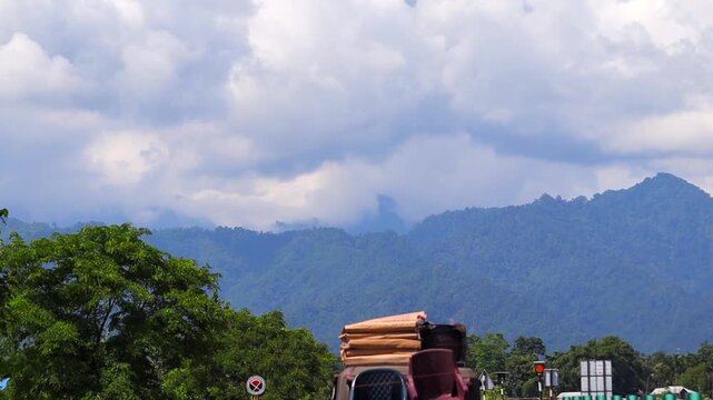 Dibrugarh, Assam, India &ndash; 23 September 2026: A loaded cargo truck travels along National Highway 515, with forest-covered mountains, road signs, utility infrastructure, and a cloudy sky