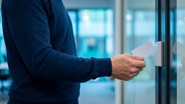 RFID card access control and contactless door entry concept, man holding blank badge card to reader on office door for building security, employee authentication and permission