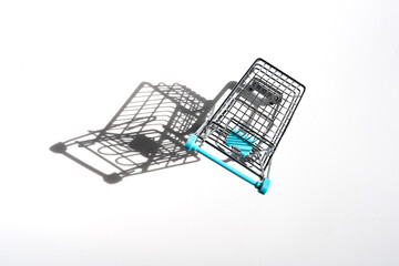 Miniature shopping cart casting a long shadow on white background, symbolizing consumerism, retail, and shopping concepts © Alberto