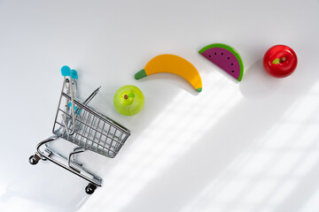Miniature shopping cart with wooden fruit toys, representing healthy eating choices and consumerism from an overhead view © Alberto