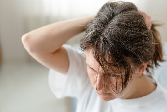 A woman gently cares for her graying silver hair with special products daily. The mature adult learns best routine to maintain strand health. Mother devotes time to her aging hair needs.
