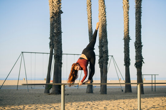 White woman exercising on balance beam at beach with palm trees