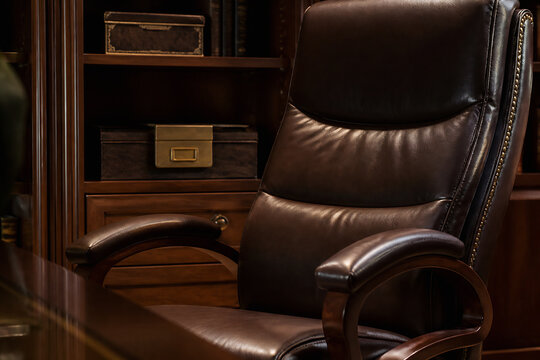 A dark brown leather executive chair is positioned in a richly furnished, dimly lit office setting.
