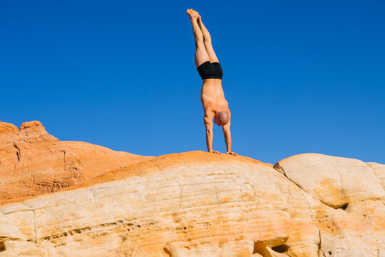 White man doing handstand exercise on rock formation outdoors