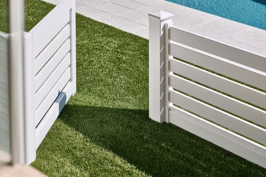 White slatted fence and gate open to bright pool and green lawn