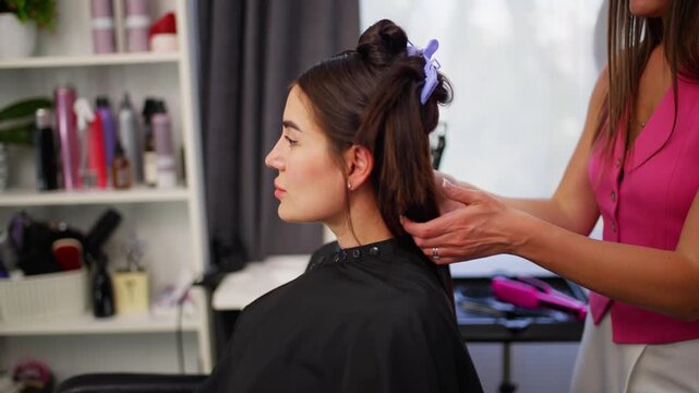 A hair stylist braids hair in a salon, showcasing professional and focused techniques from a side view. The scene highlights tools and products on a mirror, set against a clean background.