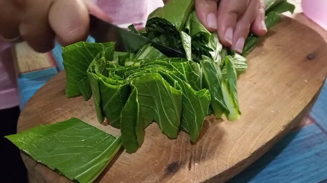 Close up of hands cutting bok choy leaves on wooden board - healthy food preparation