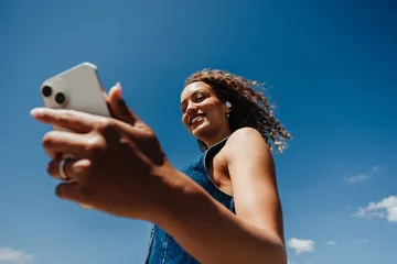 Woman checks smartphone while listening to music outdoors under blue sky © Jacob Lund
