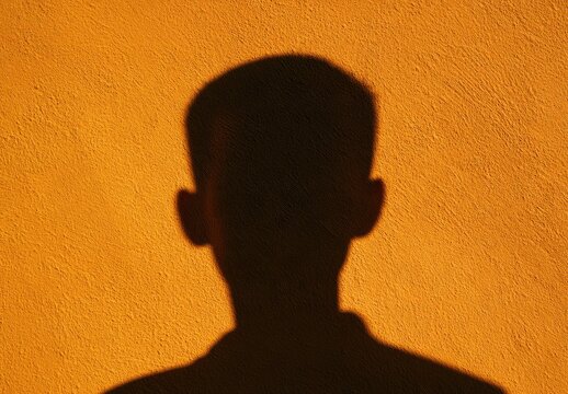 A dark silhouette of a person's head and shoulders against a textured orange wall