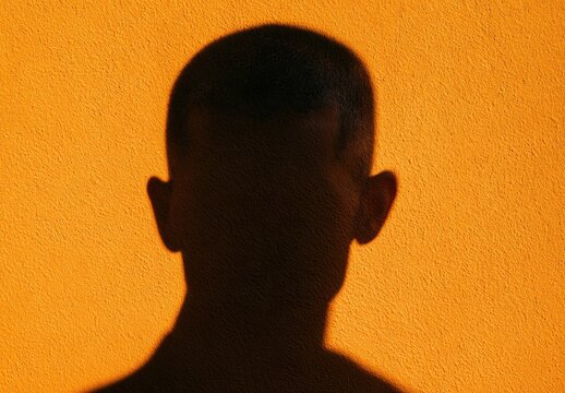 A stark silhouette of a person's head and shoulders against a textured orange wall