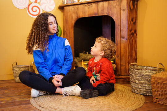 Young boy looking up at older sister in a cozy Christmas living room, sharing a warm moment
