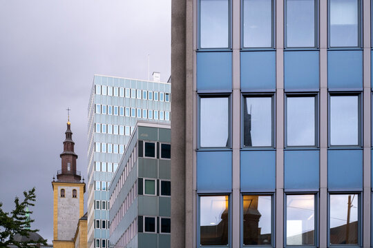 Modern office facades frame an older tower in the background, showing layered urban architecture through windows across the modern office facades