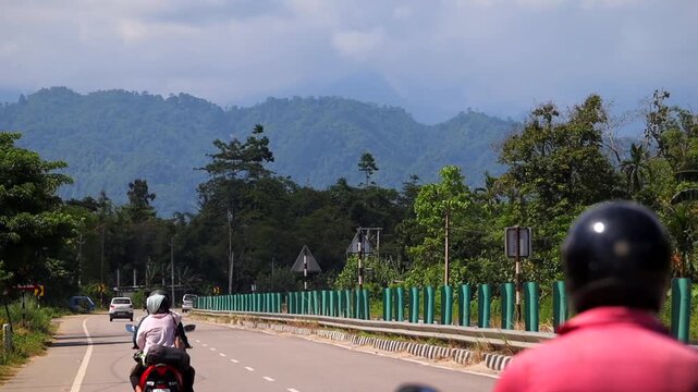 Dibrugarh, Assam, India &ndash; 23 September 2026: A busy roadway surrounded by lush greenery and forested mountains, with cars, motorcycles, roadside barriers, traffic signs
