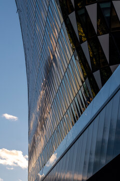 Reflective glass facade rises beside blue sky, with modern architecture using diagonal perspective and windows across the reflective glass facade