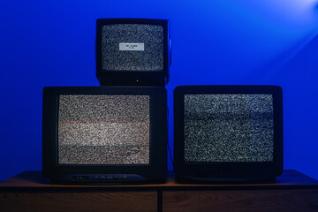 Plakat Three vintage CRT televisions displaying static noise and no signal under dramatic blue lighting