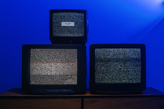 Three vintage CRT televisions displaying static noise and no signal under dramatic blue lighting