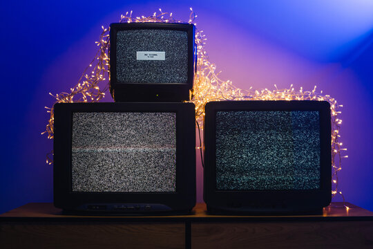 Vintage CRT televisions showing static among glowing holiday lights and decorations