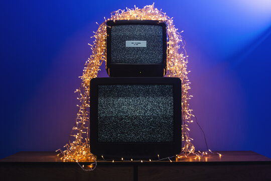 Vintage CRT televisions showing static among glowing holiday lights and decorations