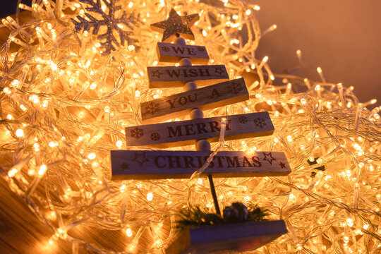 Wooden tree ornament with Merry Christmas message surrounded by glowing warm fairy lights