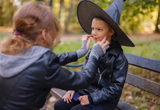 Mother and daughter prepare for Halloween walk in autumn park, wearing witch hats and holding jack o lantern, surrounded by colorful foliage in Zagreb in Croatia sunny October day.