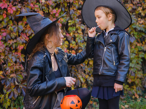 Mother and daughter go trick or treating down residential street during Halloween. Family holds pumpkin lanterns passing decorated autumn houses in Zagreb Croatia