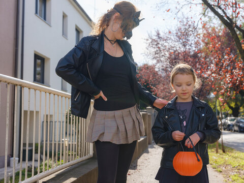 Mother and daughter go trick or treating down residential street during Halloween. Family holds pumpkin lanterns passing decorated autumn houses in Zagreb Croatia
