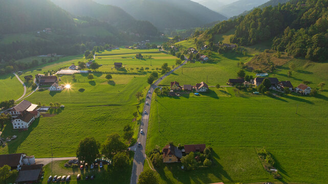 High angle drone shot of Ljubno ob Savinji, Slovenia. Scenic alpine village, Savinja river valley, green agricultural fields, traditional houses with red roofs, church.