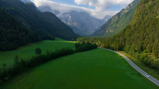 Majestic view of Logar Valley in Slovenia. Deep green forested valley stretches towards giant Kamnik Savinja Alps mountains covered with white clouds under blue sky.