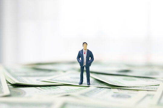 A business figure standing on a pile of US dollar banknotes. Concepts of financial success, investment planning, and business growth.