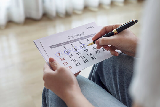Woman holding calendar and marking dates with pen. Concept of schedule planning, event reminder, appointment, deadline, and time management.