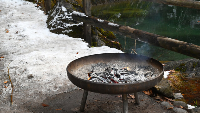 Outdoor metal fire pit with smoldering embers in snow near lake Blausee Switzerland