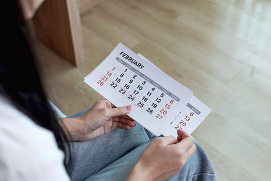Woman holding February calendar with marked cycle dates. Concept of period cycle tracking, menstrual health, ovulation, fertility, and women healthcare.