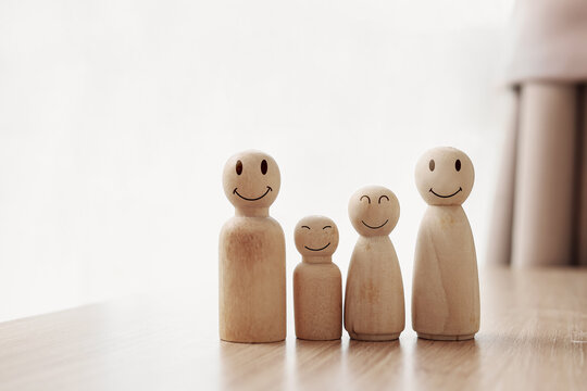 Happy wooden doll family with smiling faces on table with copy space. Concept of happy family, insurance, planning, togetherness, and warm home.