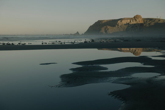 Moody low key photography of a coastal cliff reflecting in a calm tide pool on an Oregon beach