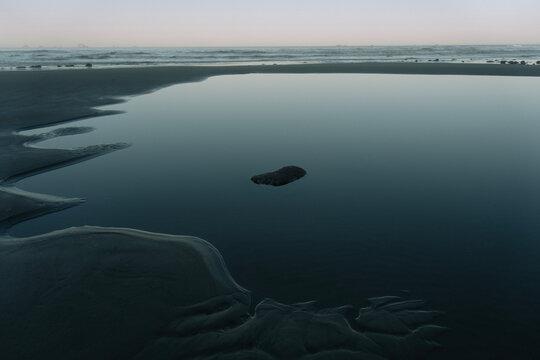 Moody low key photography of a minimalist tide pool on a dark sandy Oregon beach