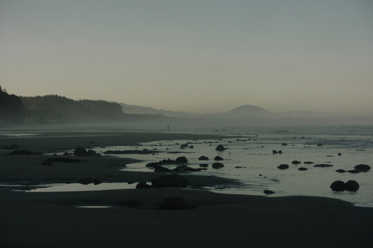 Moody low key photography of a wide misty beach and rocky shoreline along the Oregon coast