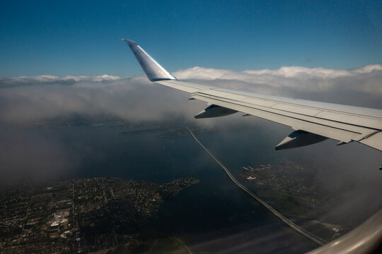 Airplane wing flying high above clouds and a long bridge over the water