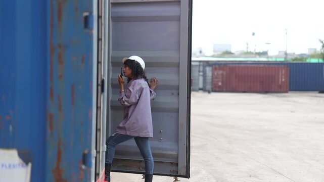A female container inspector leans against an open container door while reporting an inspection result on her two way radio during a routine shift at the container terminal.