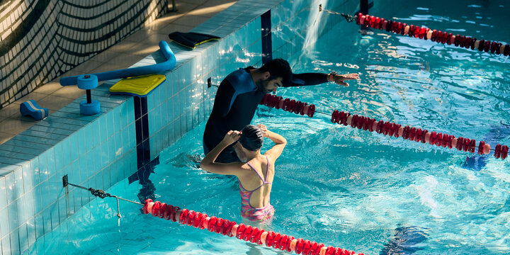 Male trainer guides child through swimming drill in indoor lane with focused care. Youth sports, water confidence, active childhood concept.